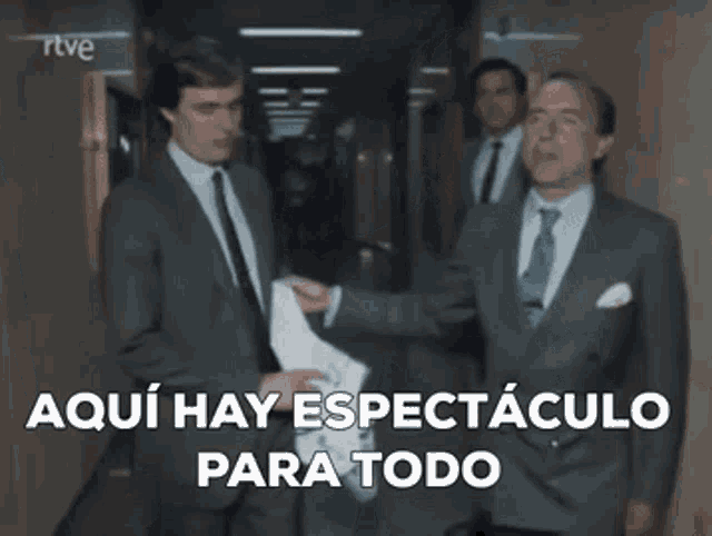 a group of men in suits and ties are walking down a hallway and one of them is holding a piece of paper .