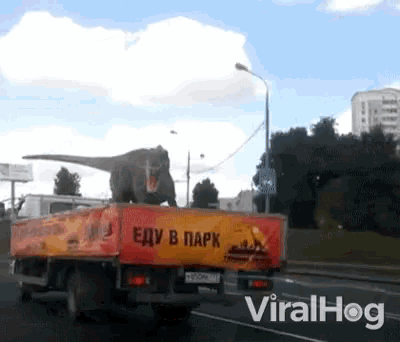 a truck with a t-rex on the back is driving down a road