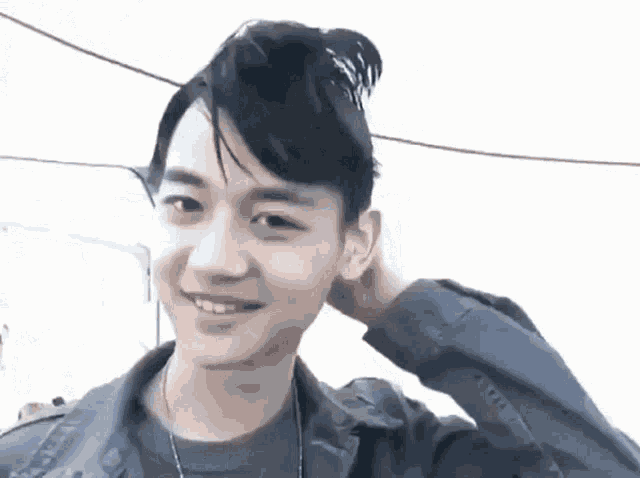 a young man with his hair in a bun is smiling and holding his hand to his ear .