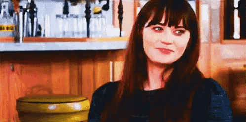 a woman with long hair and bangs is standing in front of a bar and smiling .