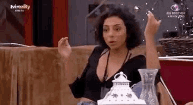 a woman is sitting at a table with a vase in front of her and making a funny face .