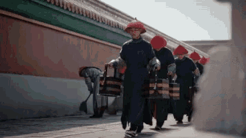 a group of men wearing red hats are walking down a sidewalk carrying buckets .