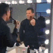 a man is applying makeup in front of a mirror with lights