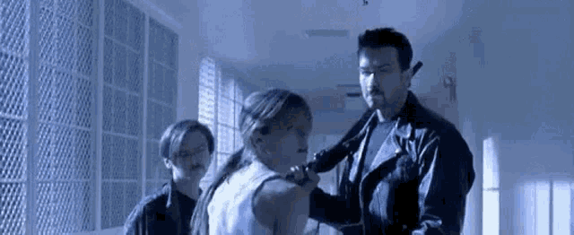 a man in a leather jacket is holding a gun in a hallway while a woman holds a gun .