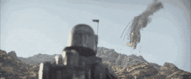 a person in a helmet is standing in front of a mountain with a rocket flying in the sky .