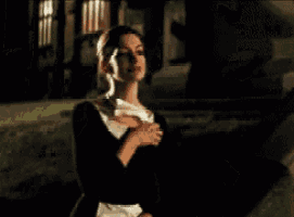 a woman in a black dress and white collar is standing in the dark holding a piece of paper .