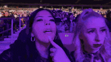 two women are sitting in front of a crowd at a concert and one of them is pointing at something .