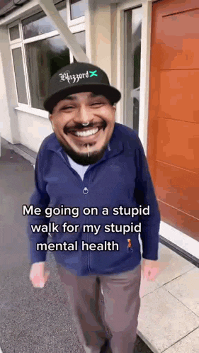 a man wearing a hat and a blue jacket is walking down a sidewalk and smiling .