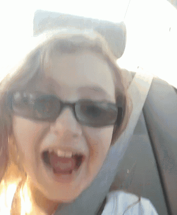 a girl wearing sunglasses is sitting in a car seat with her mouth open