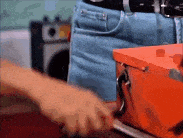 a man in blue jeans is standing next to an orange toolbox