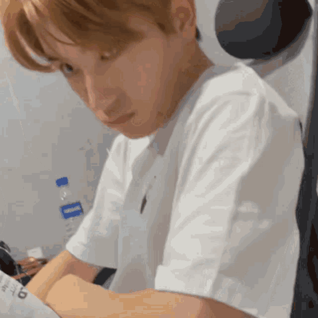a man in a white t-shirt is sitting at a desk with a bottle of water in front of him