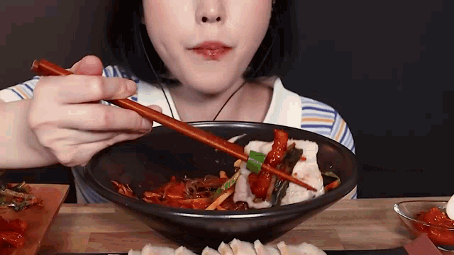 a woman is holding chopsticks over a bowl of food .