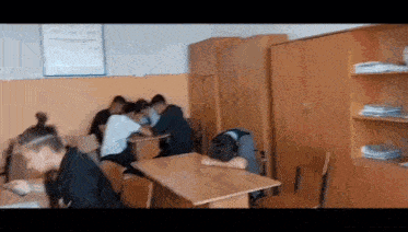 a group of students are sitting at desks in a classroom with their heads down .