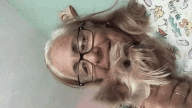 a woman wearing glasses holds a small dog in her arms .