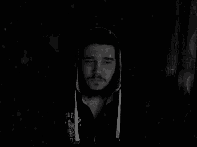 a black and white photo of a man with a beard wearing a hoodie in the dark .