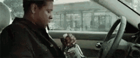 a man is sitting in the driver 's seat of a car eating a sandwich and drinking water .