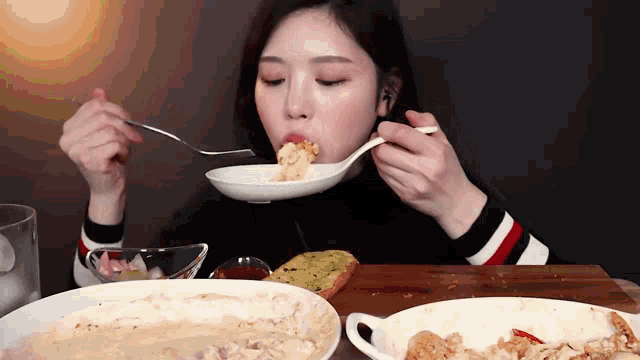 a woman is eating a bowl of food with a fork and spoon