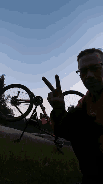 a man giving a peace sign with a bicycle in the background