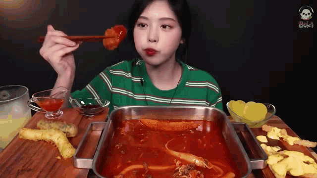 a woman in a green striped shirt is eating food with chopsticks ..
