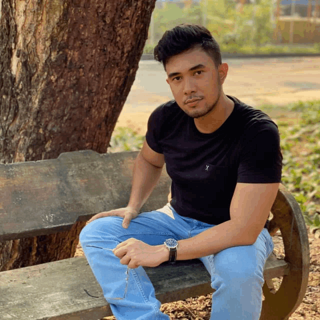 a man wearing a watch sits on a bench in front of a tree