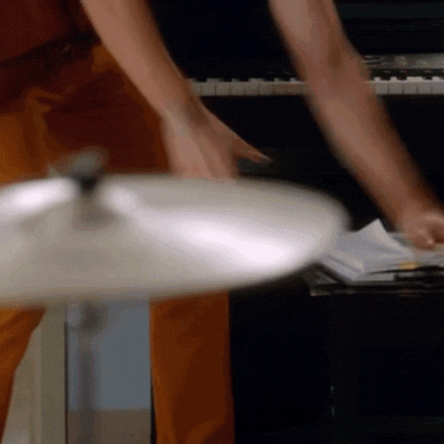 a man in orange pants is playing a cymbal in front of a piano
