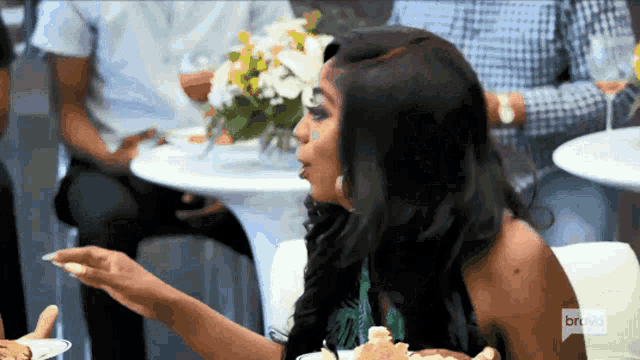a woman sitting at a table with a plate of food and a bravo logo on her shirt