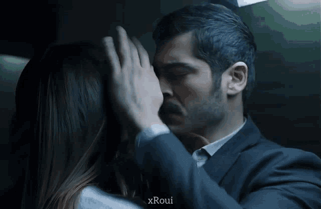 a man and a woman are kissing with the name xroui on the bottom right