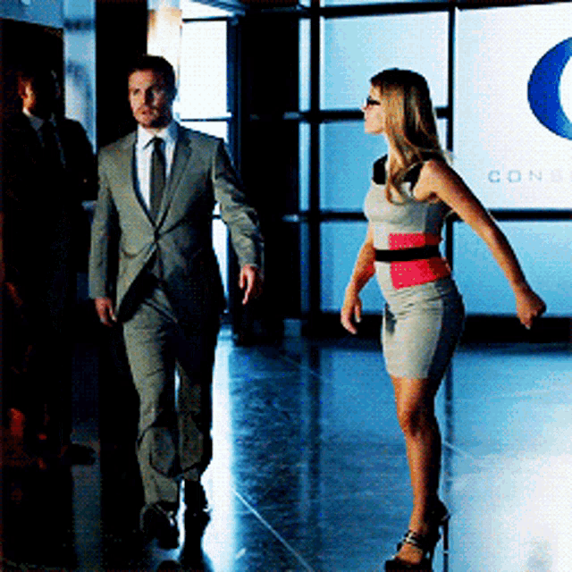 a man in a suit and tie walks with a woman in a dress in front of a sign that says cone