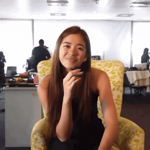 a woman is sitting in a chair with a phone in her hand and smiling