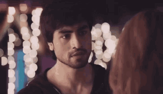 a man and a woman are looking at each other in front of a blurry background of lights .
