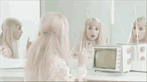 a woman in a white dress is sitting in front of a mirror looking at herself in the mirror .