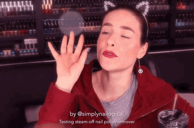 a woman wearing a cat ear headband and a red jacket is testing a steam-off nail polish remover