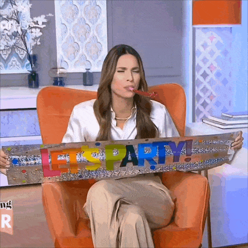a woman sitting in an orange chair holds a sign that says let 's party