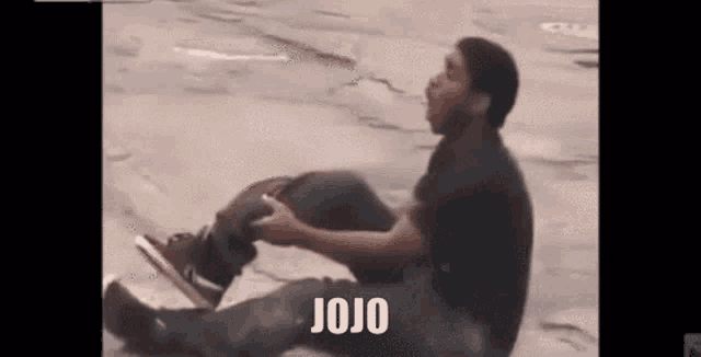 a man is sitting on the ground with his legs crossed and the words `` jojo '' written on the ground .