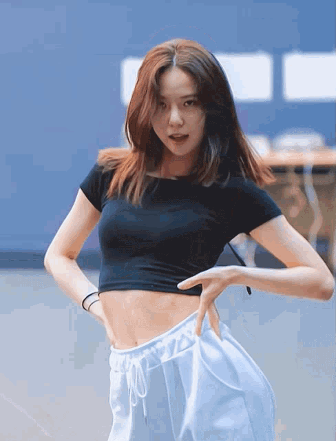 a woman in a black crop top and white sweatpants is standing with her hands on her hips