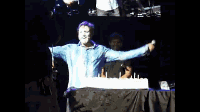 a man with blue paint on his face stands in front of a cake with candles