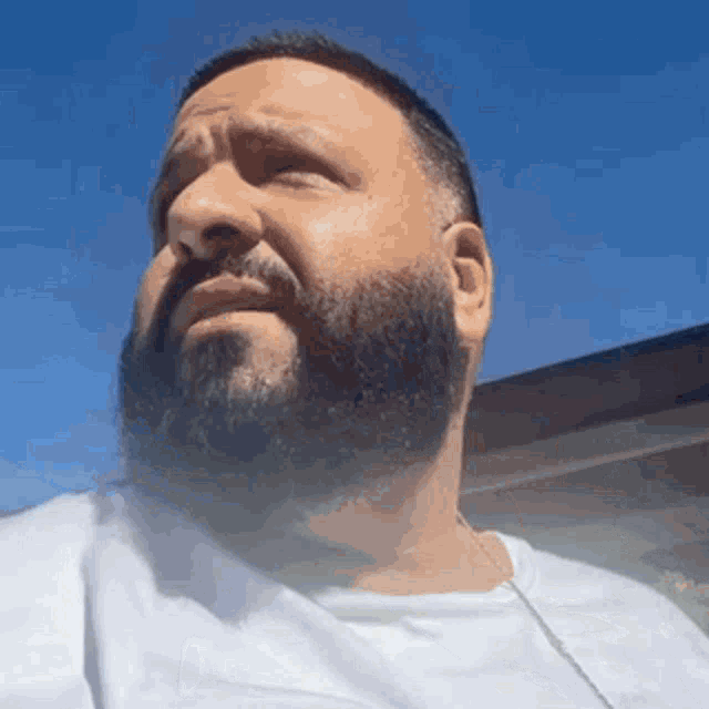 a man with a beard is wearing a white t-shirt and a chain around his neck .