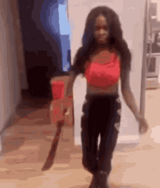 a woman in a red top and black pants is holding a large knife in her hand .