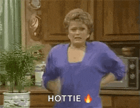 a woman in a blue shirt is standing in a kitchen with a potted plant and a microwave .