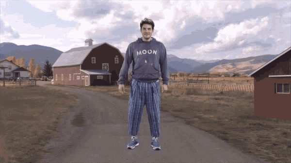 a man in a moon sweatshirt stands in front of a barn