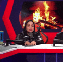 a woman is sitting at a desk with a microphone in front of a fireplace