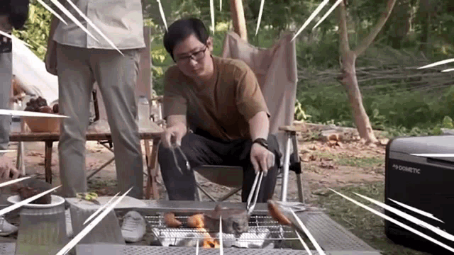 a man is sitting in a chair cooking food on a grill outside .