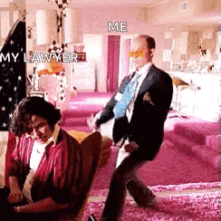 a man in a suit and tie is dancing in a living room while a woman sits in a chair .