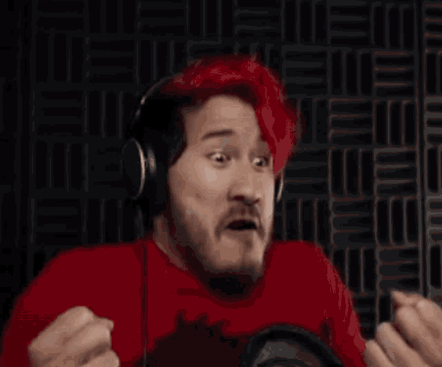 a man with red hair is wearing headphones and making a funny face while giving the middle finger .