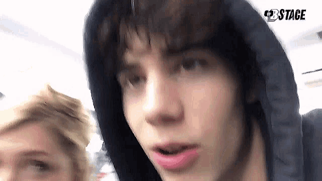 a close up of a young man wearing a hooded jacket and looking at the camera .