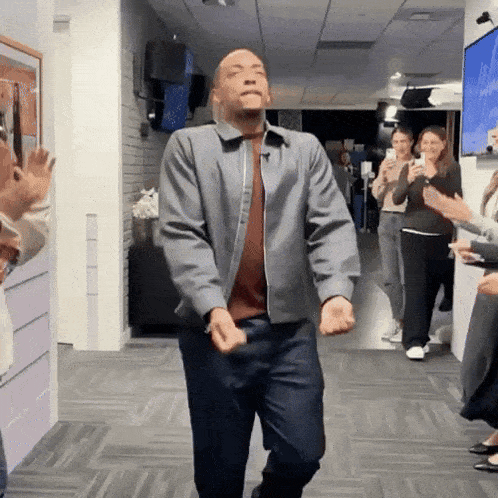 a man in a grey jacket is dancing in a hallway with people clapping behind him
