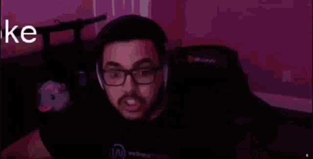 a man wearing headphones and glasses is sitting in a dark room with the word joke written on the wall .
