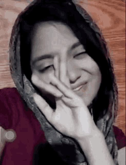 a woman is wearing a scarf around her head and making a peace sign with her hands .