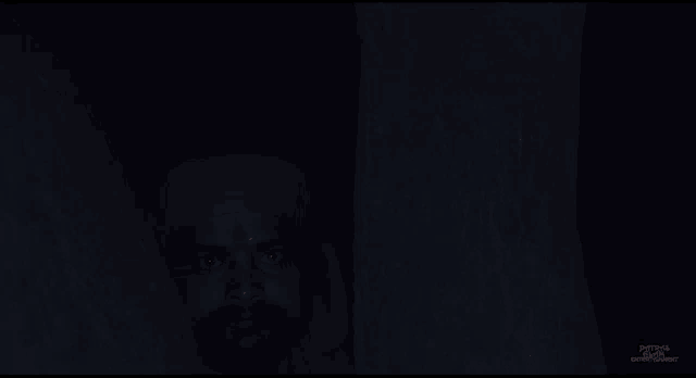 a man in a red turban with bright red eyes is standing in a dark room behind a tree