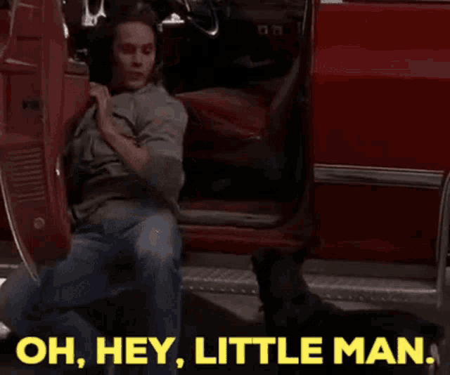 a man is kneeling down in front of a red car and says oh hey little man .
